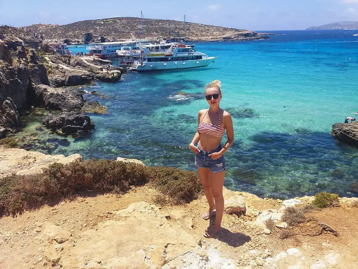 Kobieta w bikini na tle turkusowego morza i łodzi. Idealne miejsce na malta wycieczki.