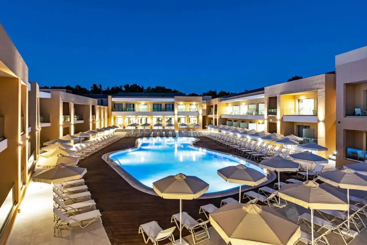 Luksusowy hotel White Olive Elite w Laganas nocą. Basen z podświetlaną wodą, leżaki i parasole. Opinie gości potwierdzają wysoki standard.