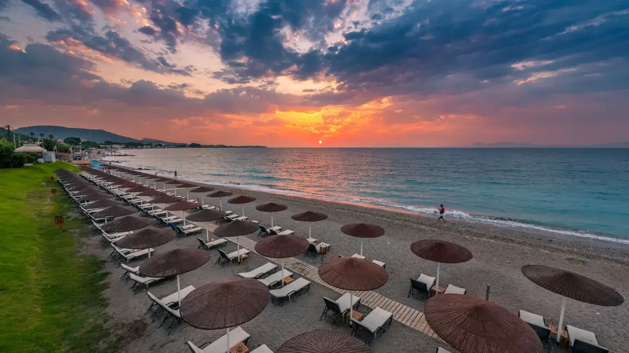 Zachód słońca nad Ixia Rodos. Pusta plaża z rzędami leżaków i parasoli, morze i malownicze chmury.