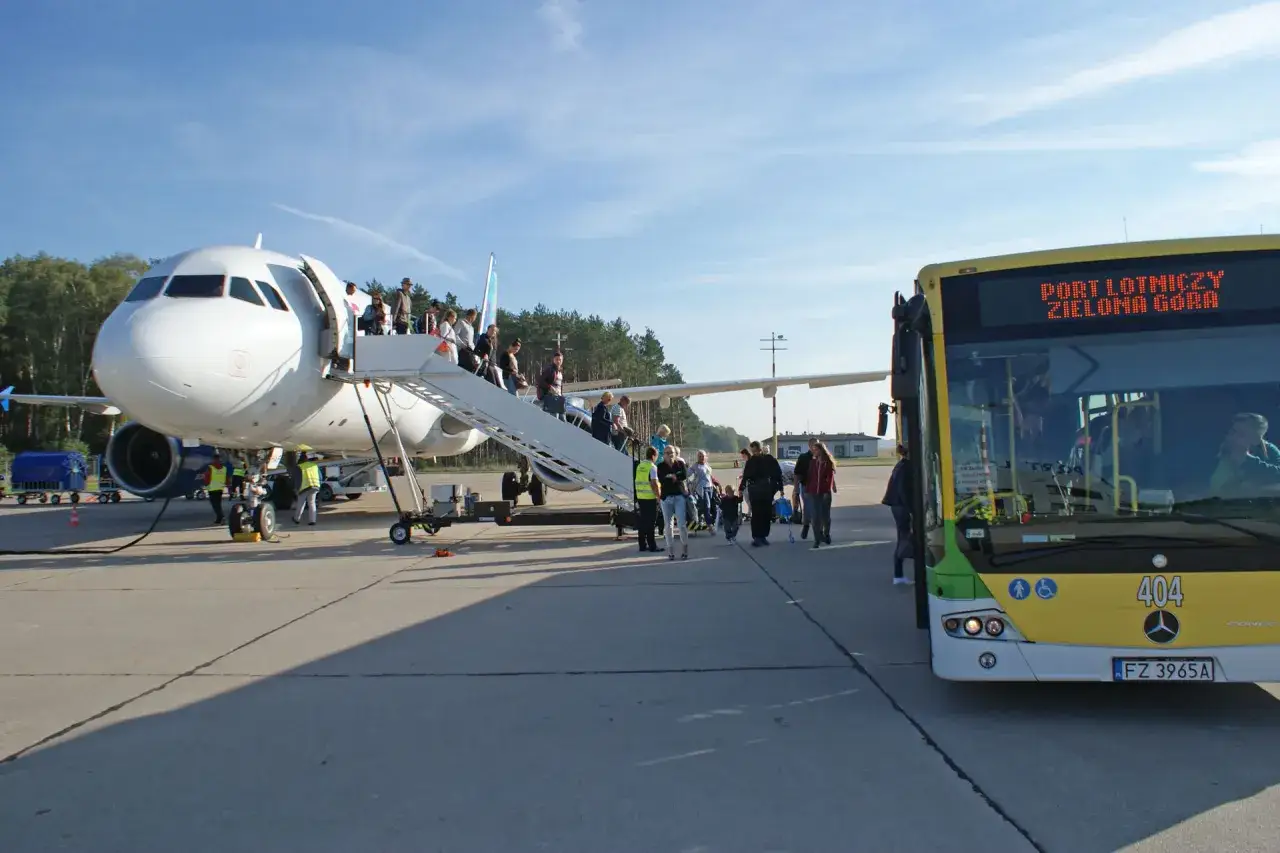 Pasażerowie wsiadają do samolotu na lotnisku Babimost. Obok stoi żółty autobus z napisem 