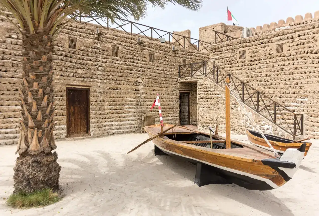 Stary Dubaj: kamienne mury, palmy i tradycyjne łodzie na piasku.