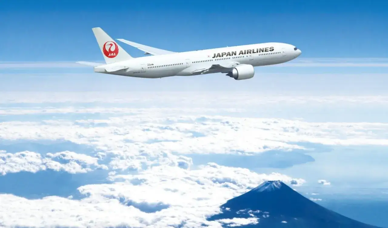 Samolot Japan Airlines leci nad chmurami, w oddali widać górę Fudżi. Zastanawiasz się, ile się leci do Japonii?