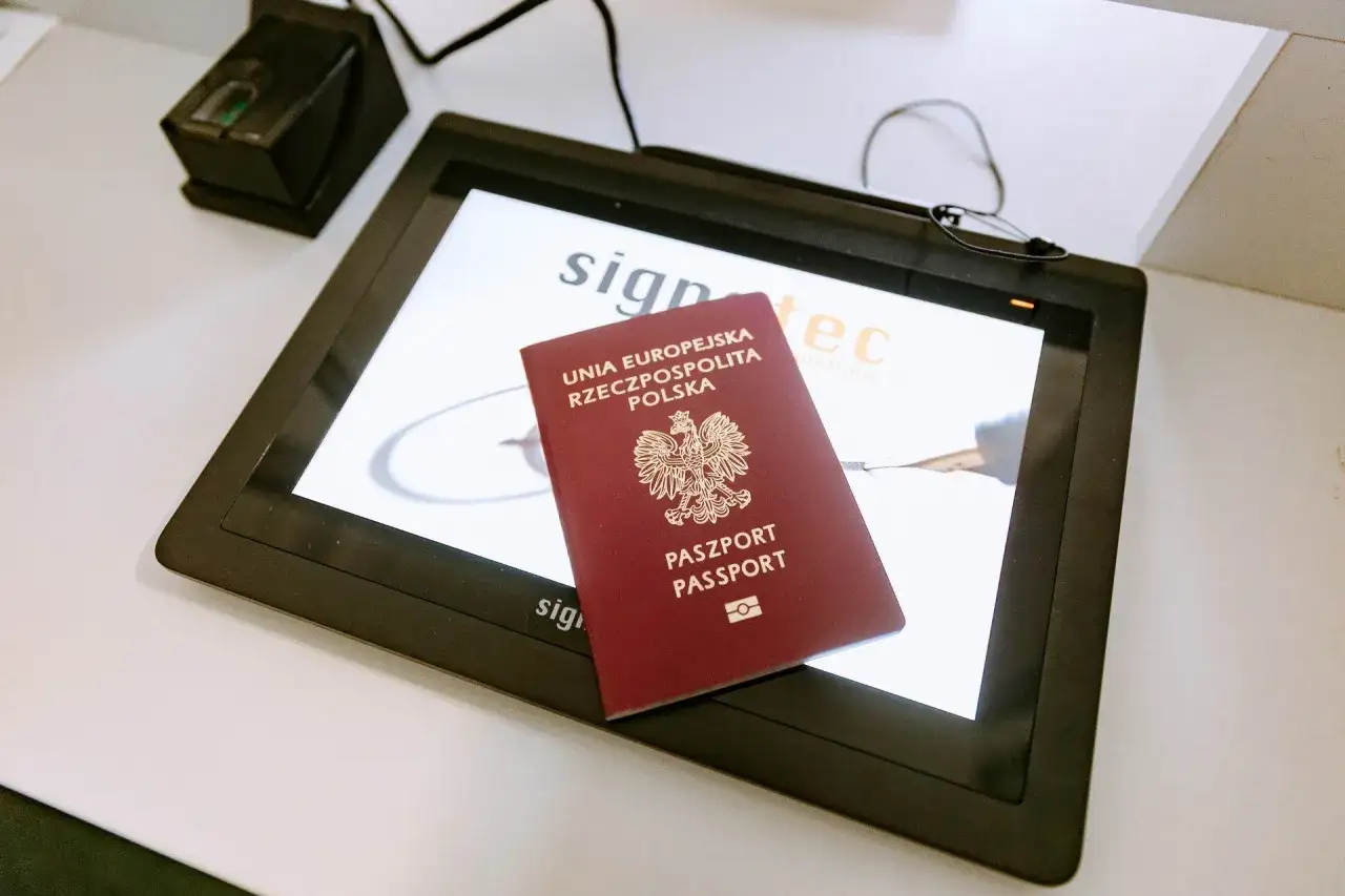Polski paszport na ekranie tabletu, obok czytnik linii papilarnych. Takie urządzenia pomagają sprawdzić, ile wyrabia się paszport.