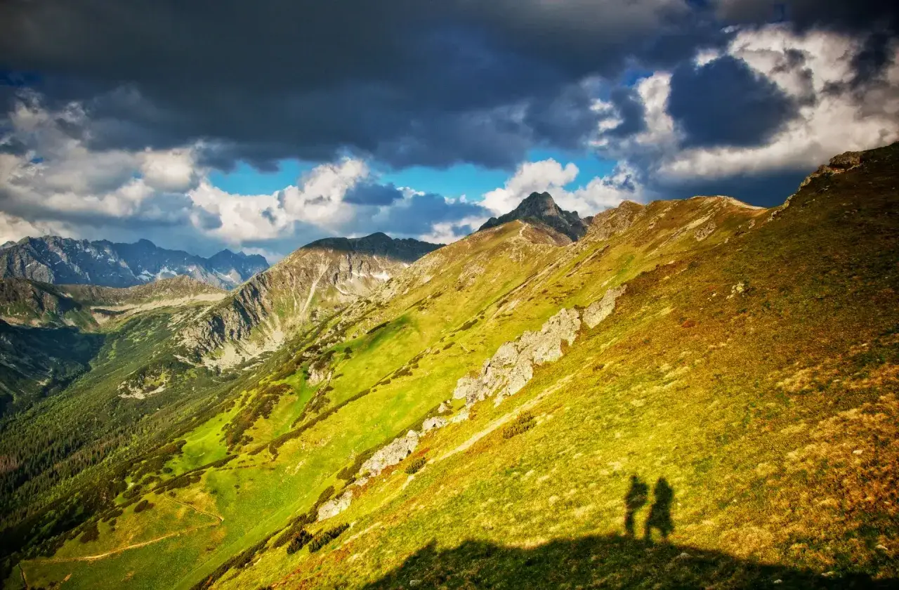 Dwie sylwetki na tle malowniczych zakopane góry. Słoneczne zbocza i burzowe chmury tworzą dramatyczny krajobraz.