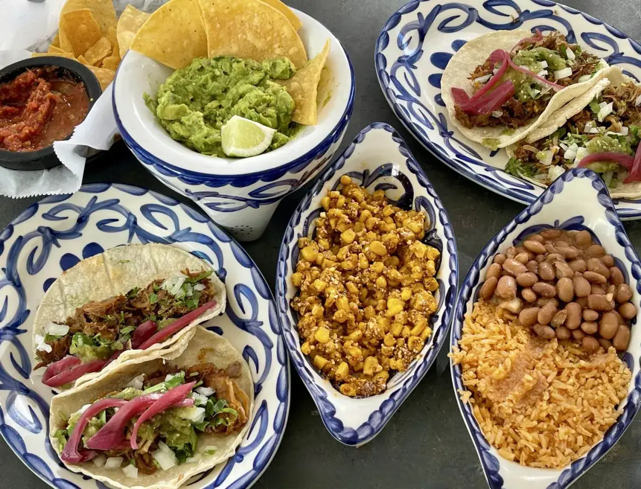 Pyszne dania meksykańskie: tacos z szarpaną wieprzowiną, guacamole, salsa, kukurydza i fasolka z ryżem.