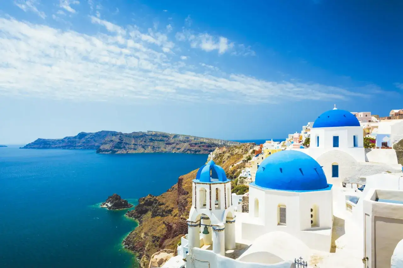 Santorini, Grecja. Białe domy z niebieskimi kopułami nad turkusowym morzem. Idealne miejsce na tanie wakacje w Grecji.