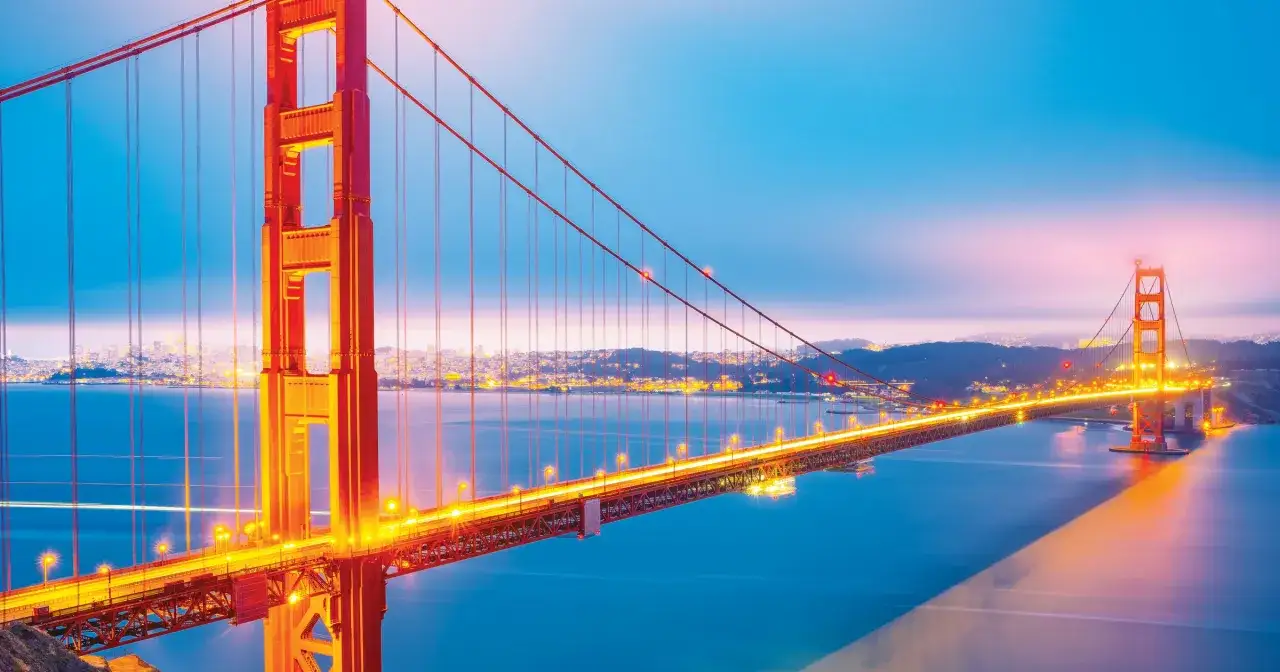 Złota Brama, most w San Francisco, lśni w blasku świateł o zmierzchu, rozświetlając wodę i miasto w oddali.