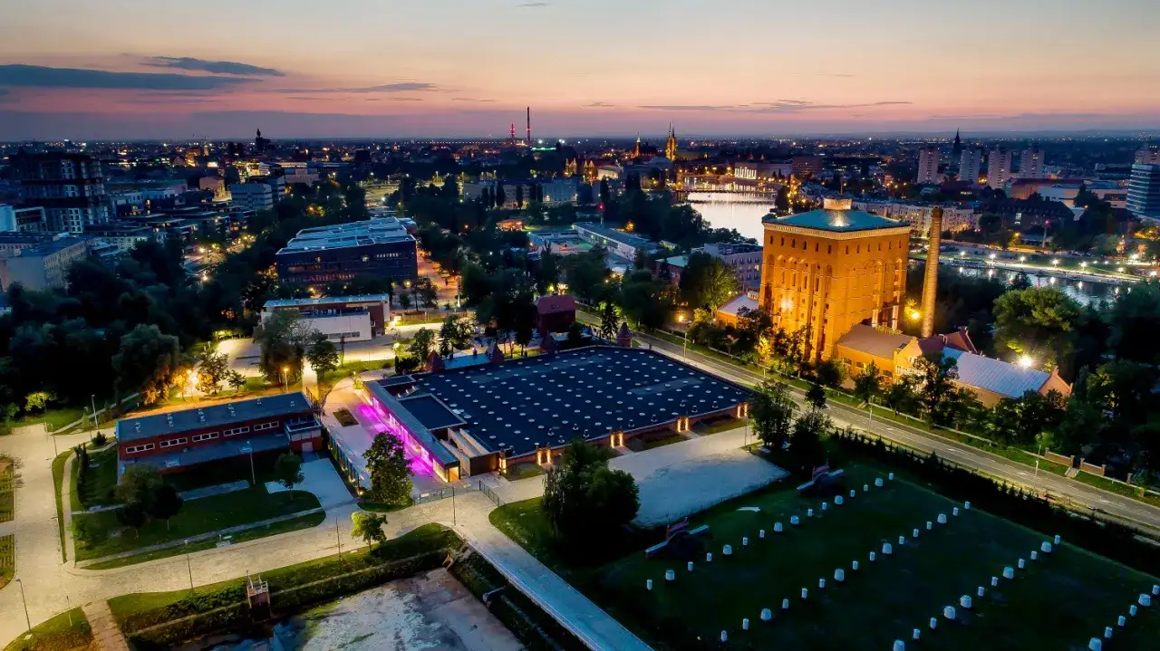 Zachód słońca nad miastem, z widokiem na nowoczesne budynki i zabytkową ceglaną wieżę. Hydropolis opinie są pozytywne, warto odwiedzić to miejsce.
