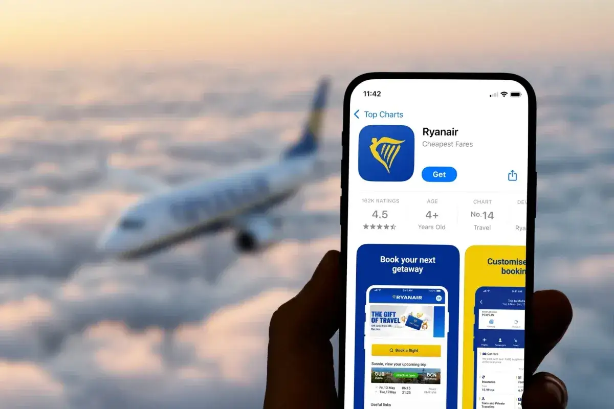 Ręka trzyma smartfon z aplikacją Ryanair, gotową do odprawy. W tle samolot leci nad chmurami.