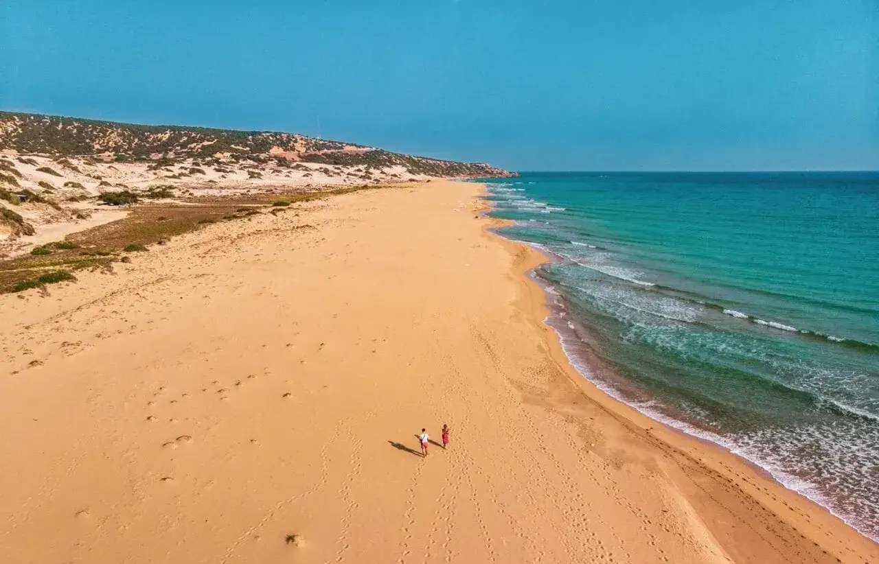 Dwie osoby spacerują po piaszczystej plaży z turkusową wodą. Czy to cypr północny czy południowy?