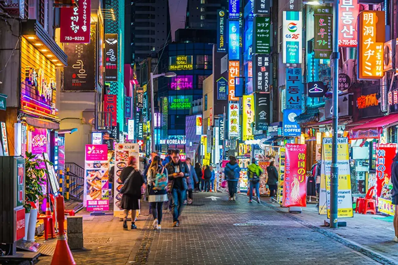 Tętniąca życiem ulica w Gangnam nocą, pełna neonowych szyldów i ludzi spacerujących po chodniku.