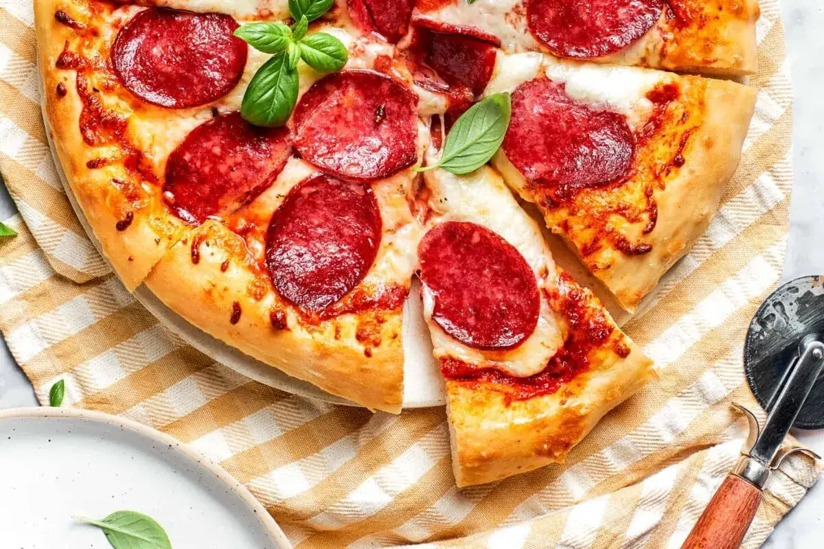 Pyszna pizza pepperoni z ciągnącym się serem i świeżą bazylią, gotowa do pokrojenia.