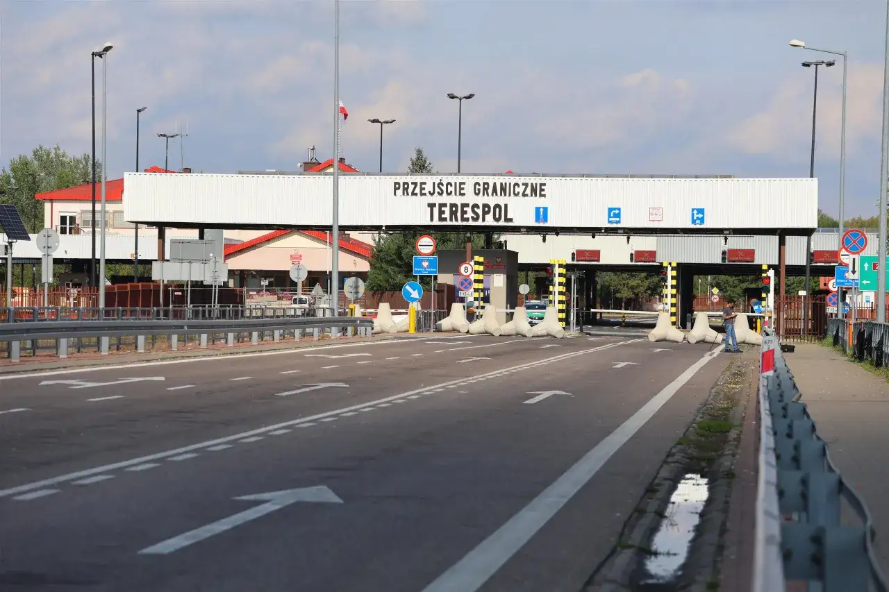 Przejście graniczne Terespol. Droga prowadzi do budynków kontrolnych, z betonowymi blokami i znakami drogowymi.