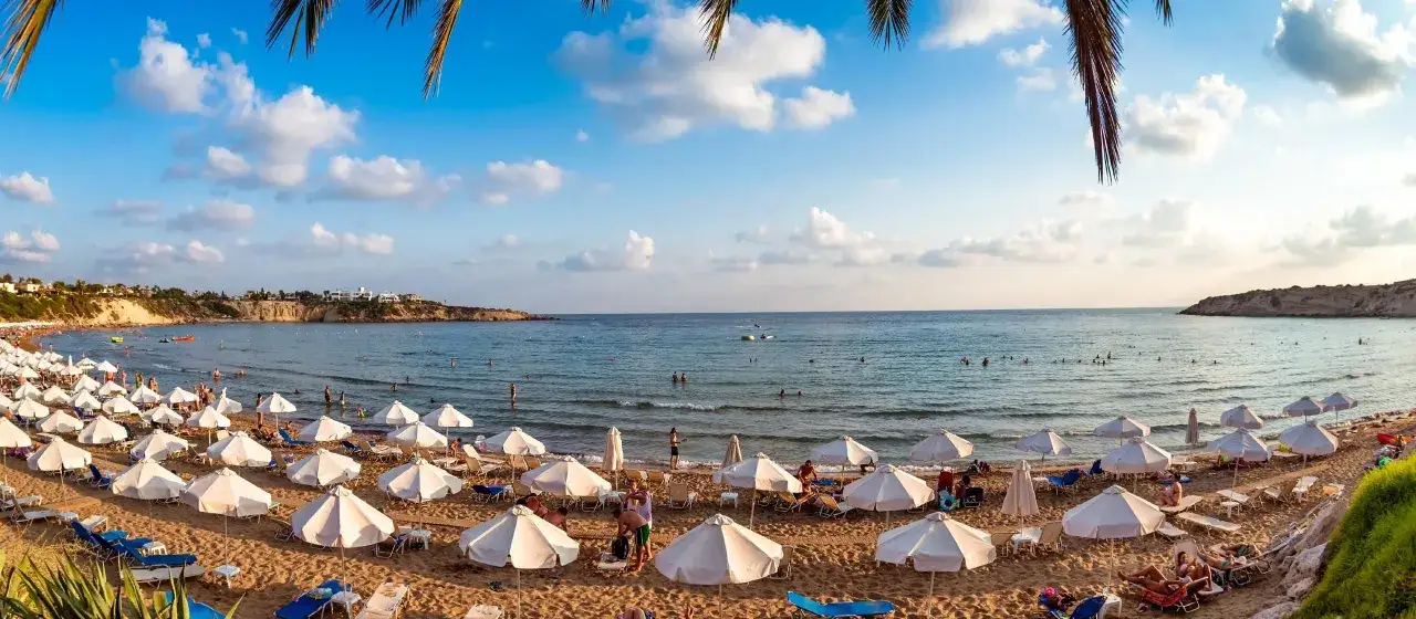 Słoneczne pafos plaże z białymi parasolami i leżakami, ludzie kąpią się w turkusowym morzu.