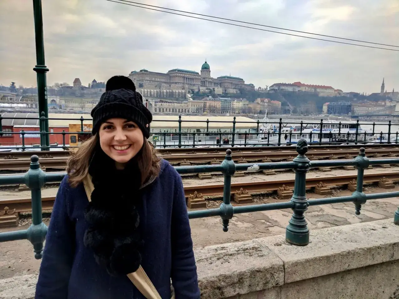 Uśmiechnięta kobieta w czapce i szaliku na tle Budapesztu. Idealne miejsce na tanie loty na weekend.