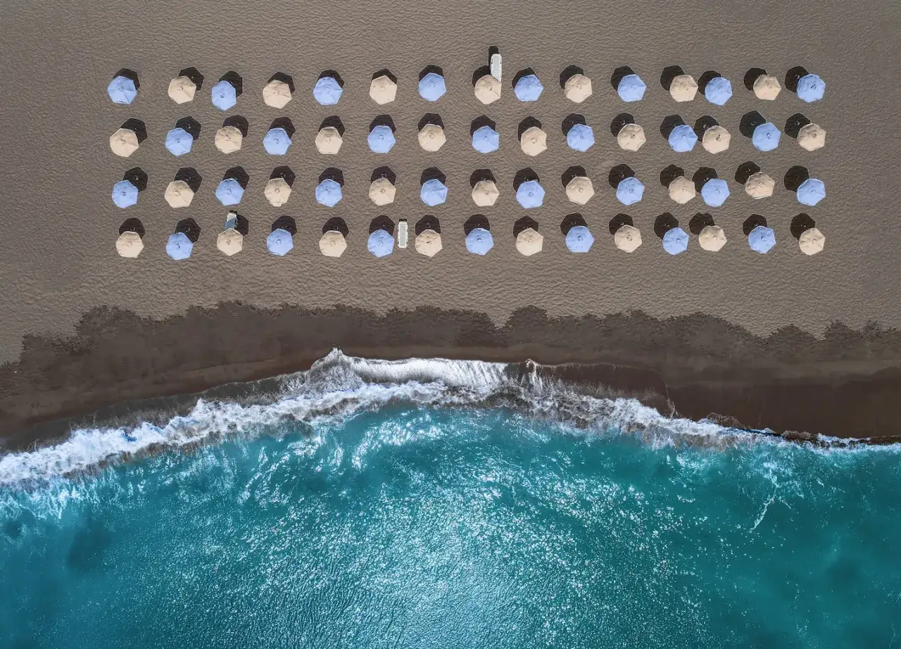 Rzędy parasoli na ciemnej plaży Santorini, obok turkusowego morza. Idealne miejsce na relaks.