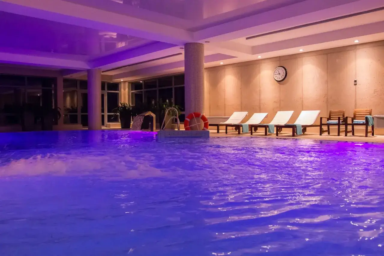 Relaksacyjny basen z fioletowym podświetleniem, leżaki i krzesła czekają na idealny weekend w spa dla dwojga.