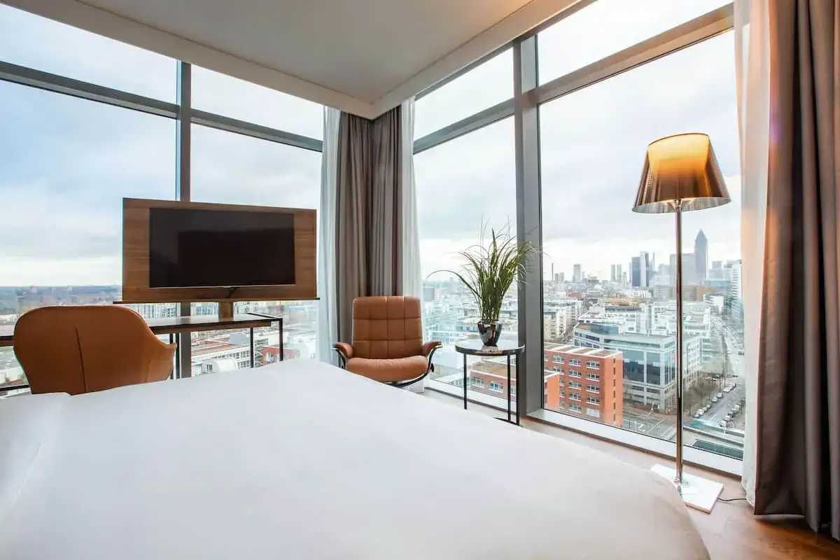 Pokój w hotelu Frankfurt Radisson Blu z widokiem na miasto, łóżko, fotele i telewizor.