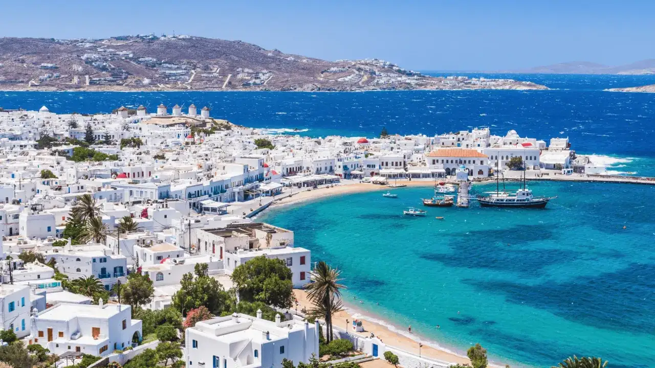 Malownicze białe domki i wiatraki na Mykonos, idealne na tanie wakacje w Grecji. Turkusowe morze i plaża zapraszają do odpoczynku.