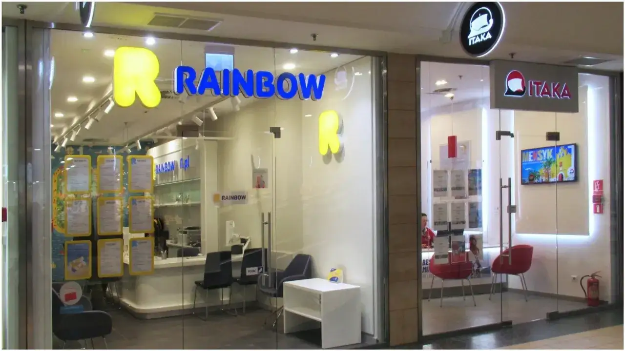 Biuro podróży Rainbow i Itaka. W witrynie Rainbow wiszą żółte plakaty z napisami, a obok logo