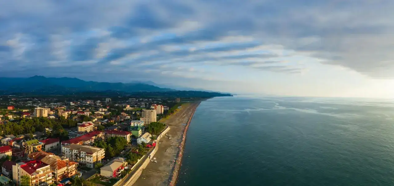 Widok z lotu ptaka na wybrzeże Gruzji. Miasto z czerwonymi dachami i zielenią, plaża pełna ludzi i spokojne morze.