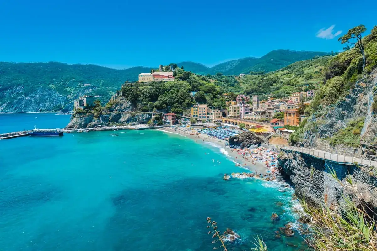 Malowniczy widok na zatokę z plażą w Monterosso, Liguria. Kolorowe domy wznoszą się na zboczu, a turkusowe morze zaprasza do kąpieli. Idealne miejsce na wakacje, jakbyś był w Mediolanie, ale na plaży.