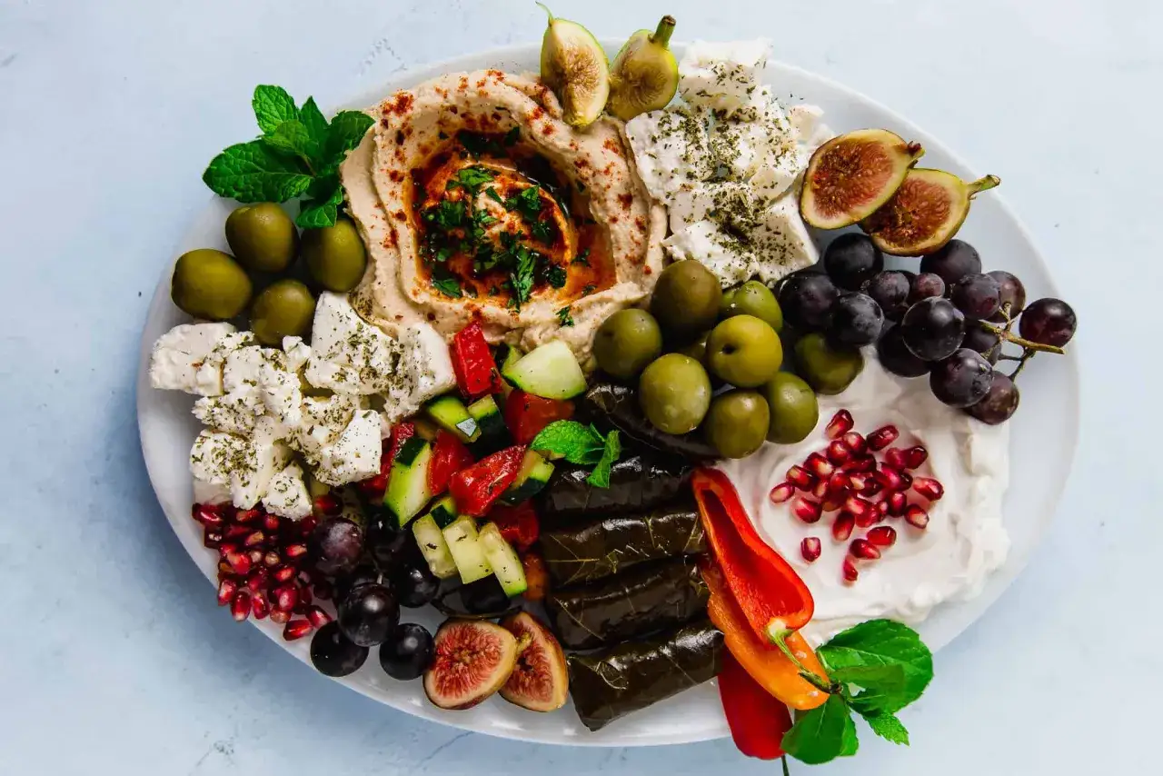 Talerz pełen śródziemnomorskich smaków: kremowy hummus, oliwki, sery, winogrona, figi, gołąbki w liściach winogron i inne pyszne meze.