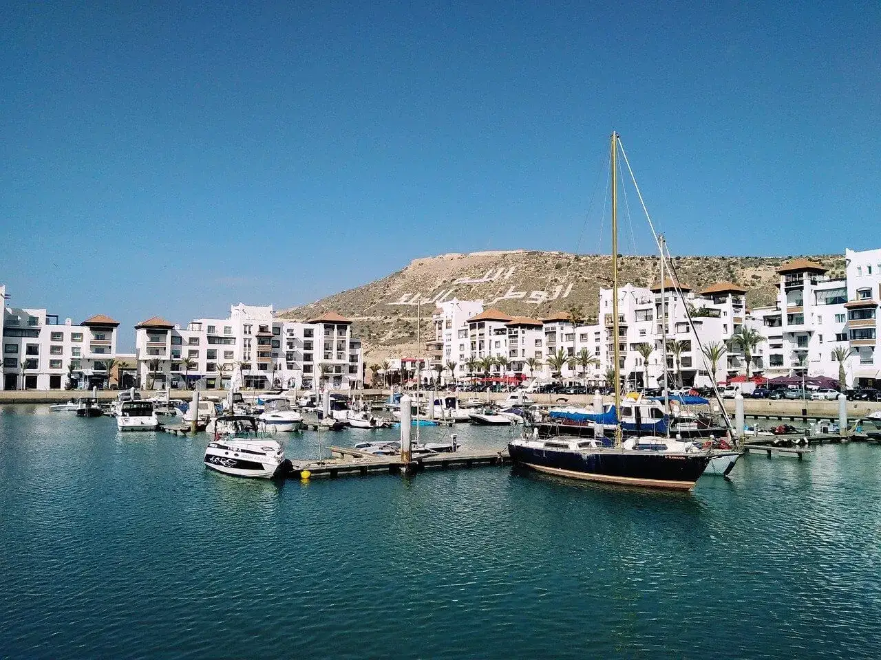Agadir pogoda marzec: słoneczny dzień w marinie, białe budynki, palmy i łodzie.