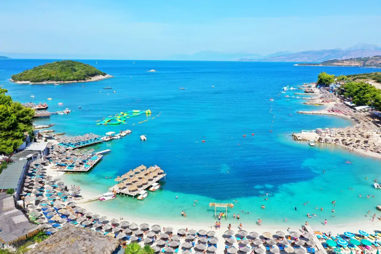 Malownicze albania plaże z turkusową wodą, wyspą, leżakami i parasolami.