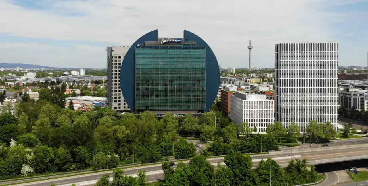 Charakterystyczny budynek hotelu Radisson Blu we Frankfurcie, otoczony zielenią i nowoczesną architekturą miejską.