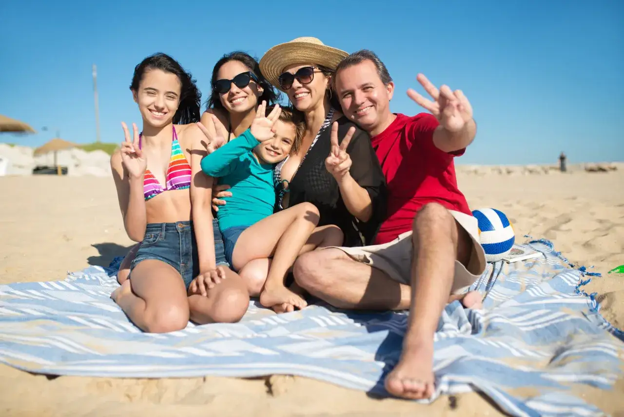 Rodzina cieszy się wakacjami all inclusive w Polsce, pozując do zdjęcia na plaży z uniesionymi dłońmi.
