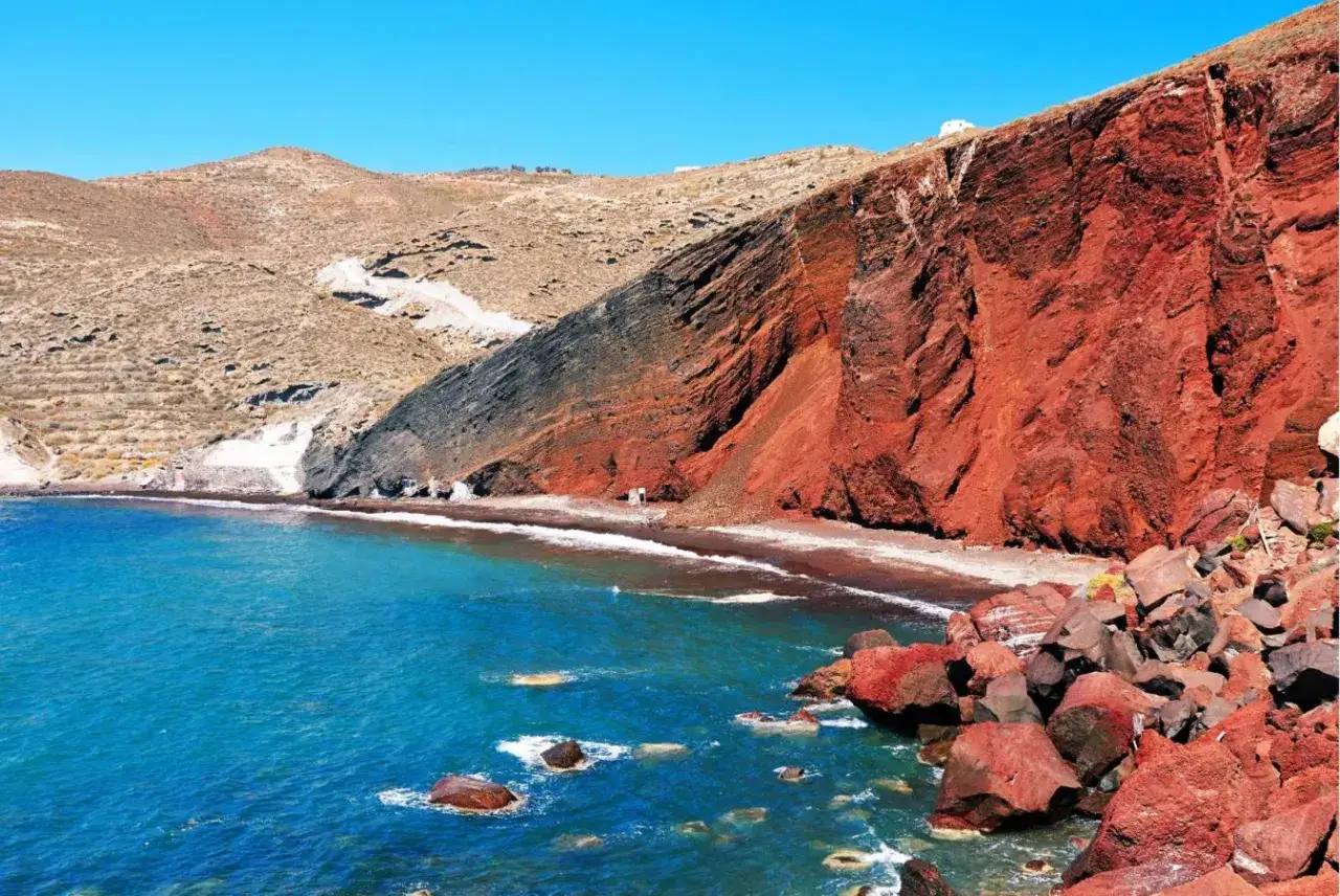 Niebieskie morze obmywa unikalne santorini plaże z czerwonymi klifami i czarnym piaskiem.