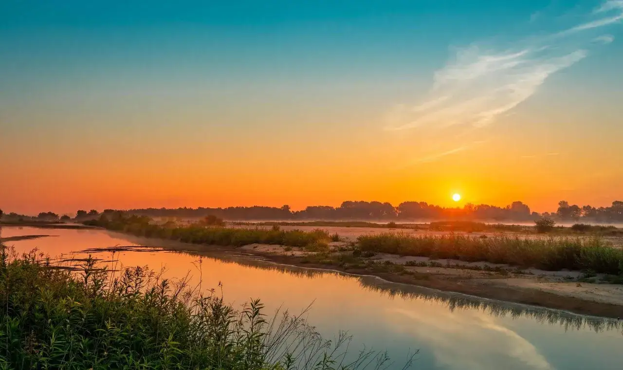 Wschód słońca nad rzeką Wisłą. Mgła unosi się nad wodą, a niebo mieni się odcieniami pomarańczu i błękitu.