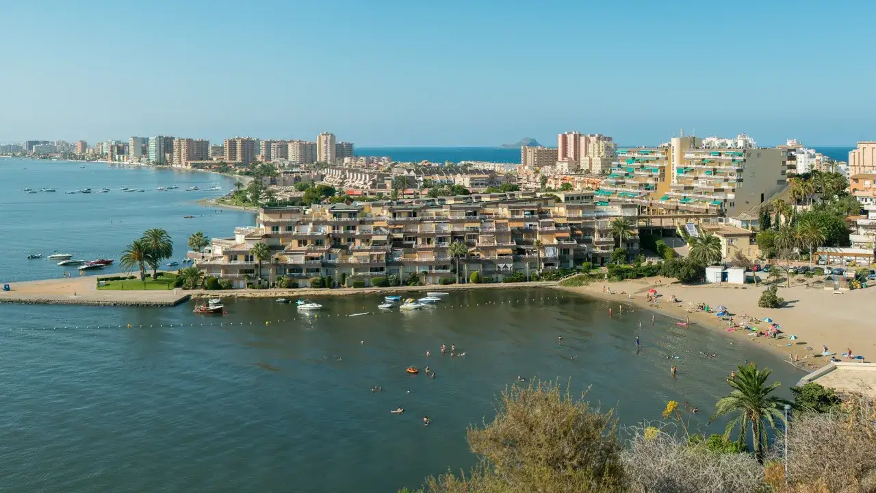 Słoneczny dzień na plaży w La Manga, Hiszpania. Ludzie kąpią się w morzu, opalają na piasku, a łodzie kołyszą się na wodzie.