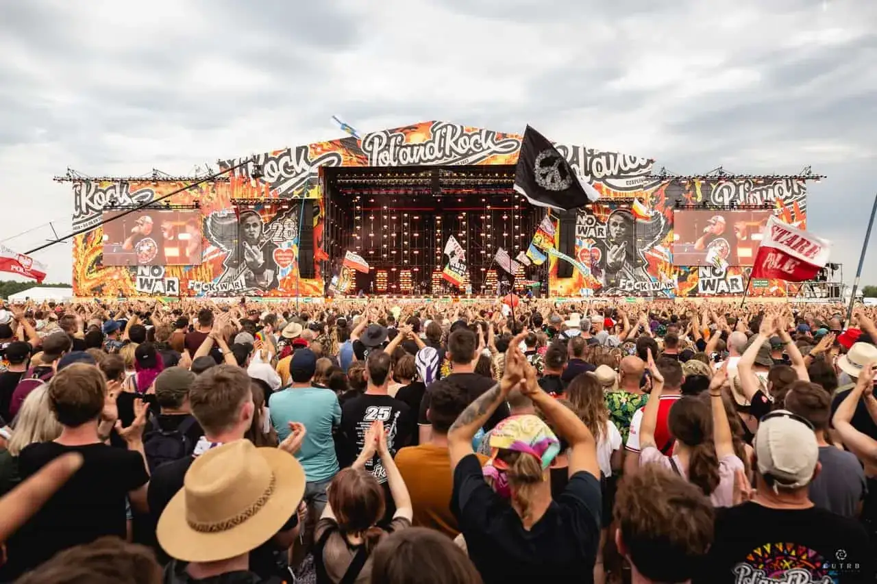 Tłum ludzi na koncercie Poland Rock, z wielką sceną w tle i transparentami