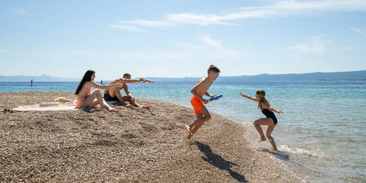 Rodzina na plaży w Chorwacji, dzieci bawią się pistoletami na wodę. Idealne miejsce, gdzie do Chorwacji z dziećmi.