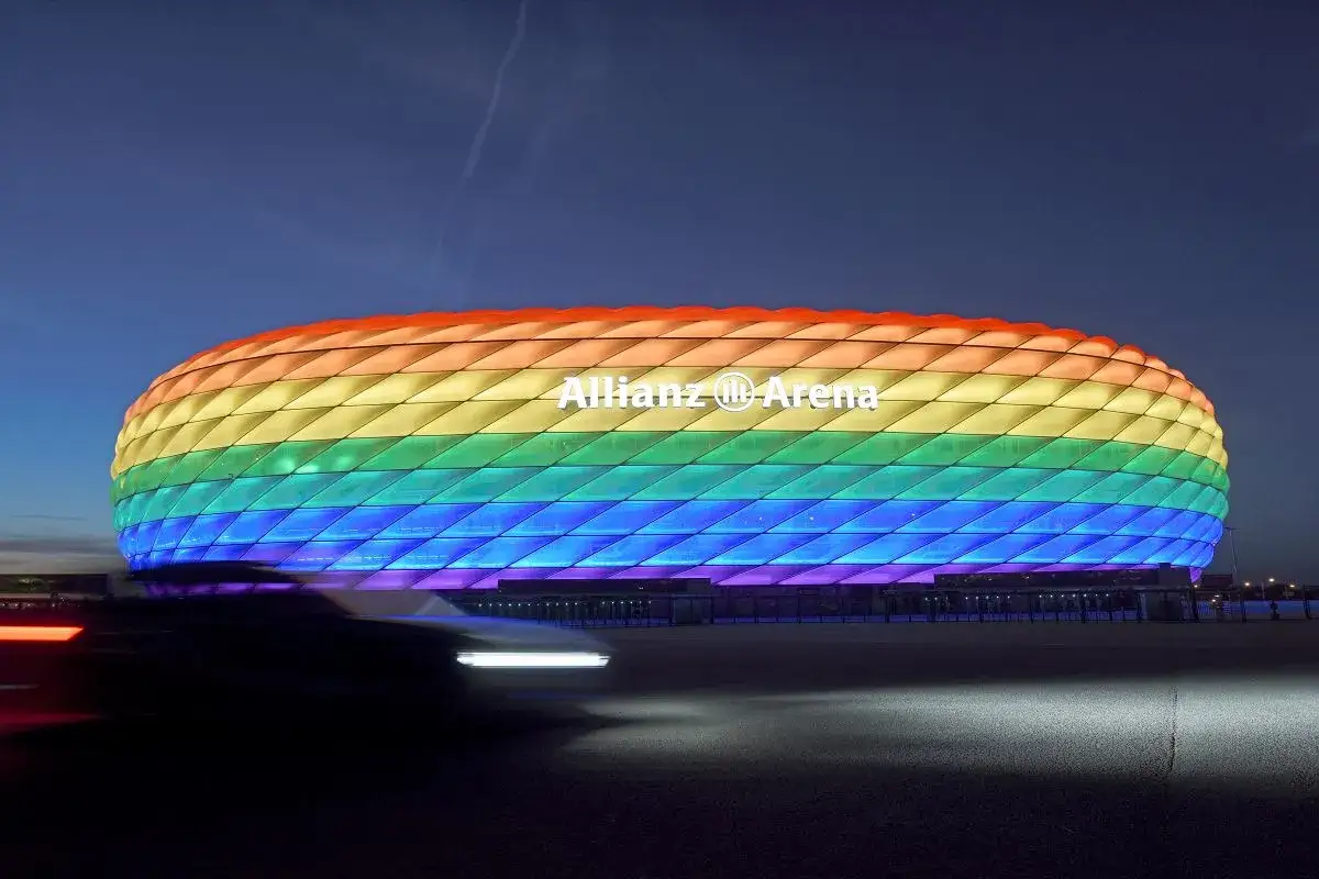 Allianz Arena w tęczowych barwach, nocą. Samochody przejeżdżają przed stadionem, zostawiając smugi światła.