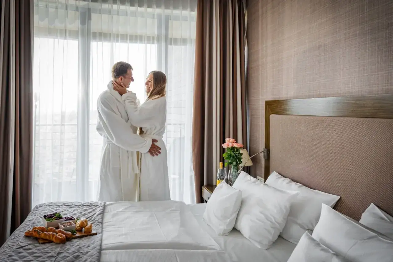 Para idealnie spędza romantyczny weekend w spa dla dwojga, przytulając się w szlafrokach. Na łóżku czeka śniadanie.