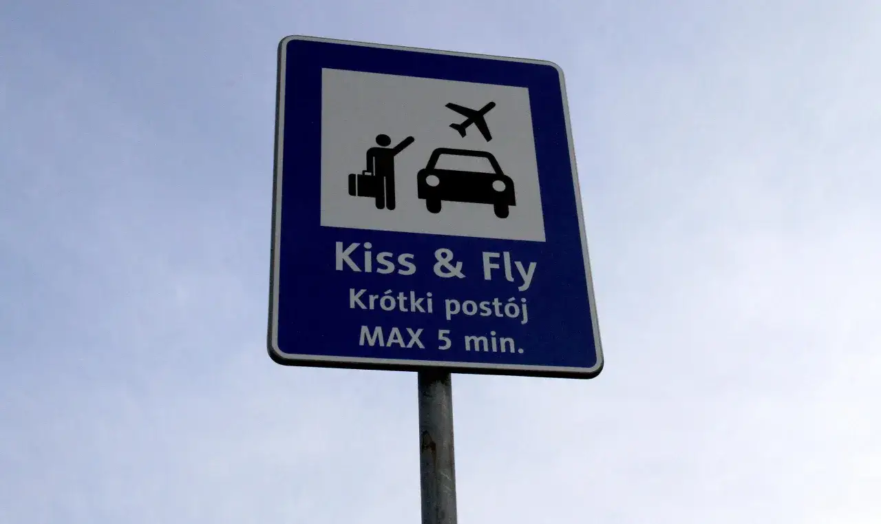 Znak Kiss & Fly: krótki postój MAX 5 min. Osoba z walizką żegna się z samochodem, by móc odlecieć.