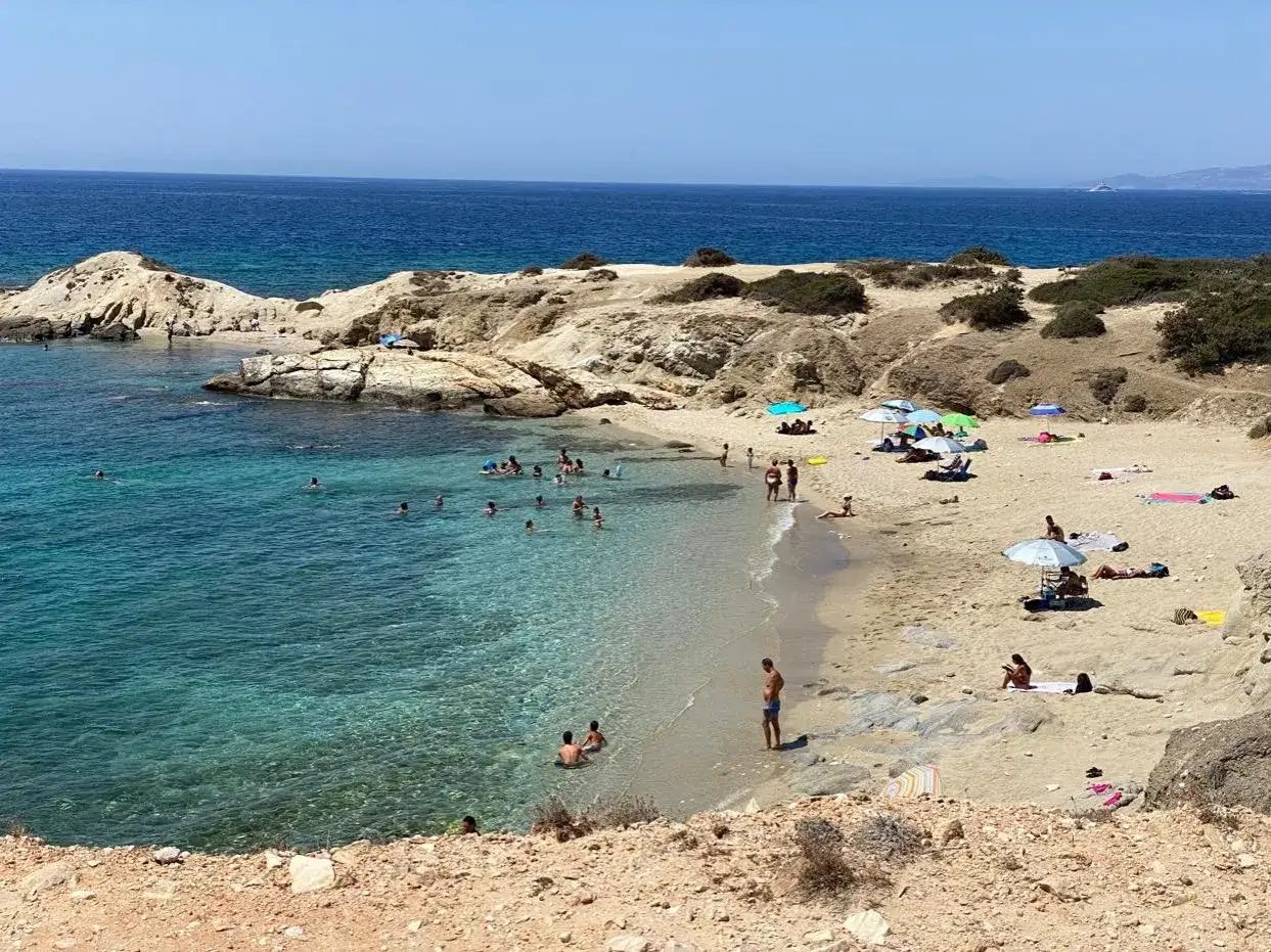 Słoneczna plaża na Naxos, z turkusową wodą i ludźmi kąpiącymi się oraz odpoczywającymi pod parasolami.