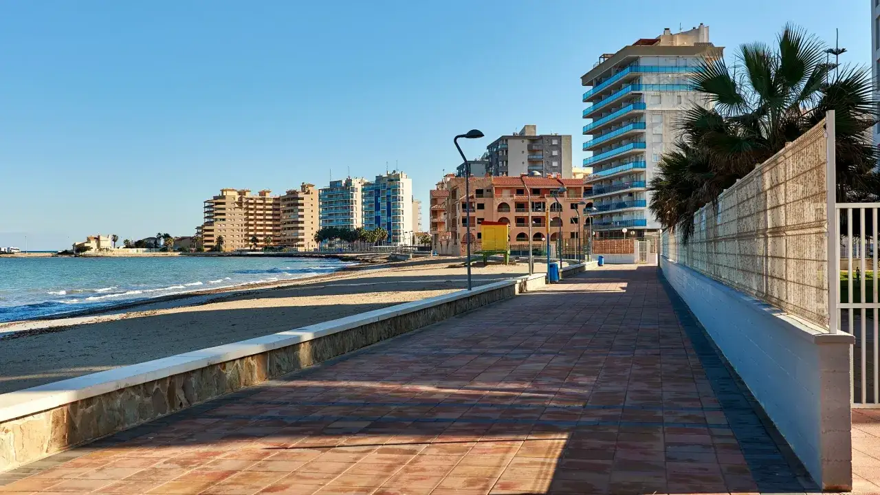Promenada nad morzem w La Manga, Hiszpania. Widok na plażę, budynki mieszkalne i błękitne niebo.