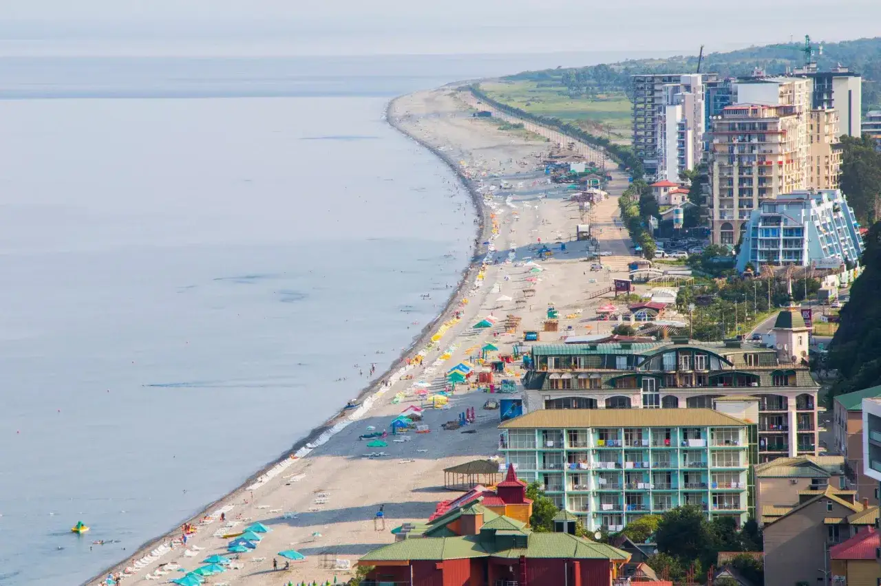 Słoneczna plaża w Gruzji nad Morzem Czarnym, pełna kolorowych parasoli i hoteli.