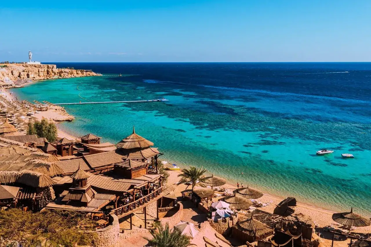 Idealna sharm el sheikh pogoda marzec: turkusowe morze, piaszczysta plaża, drewniane domki z krytymi strzechą dachami, łodzie na wodzie.