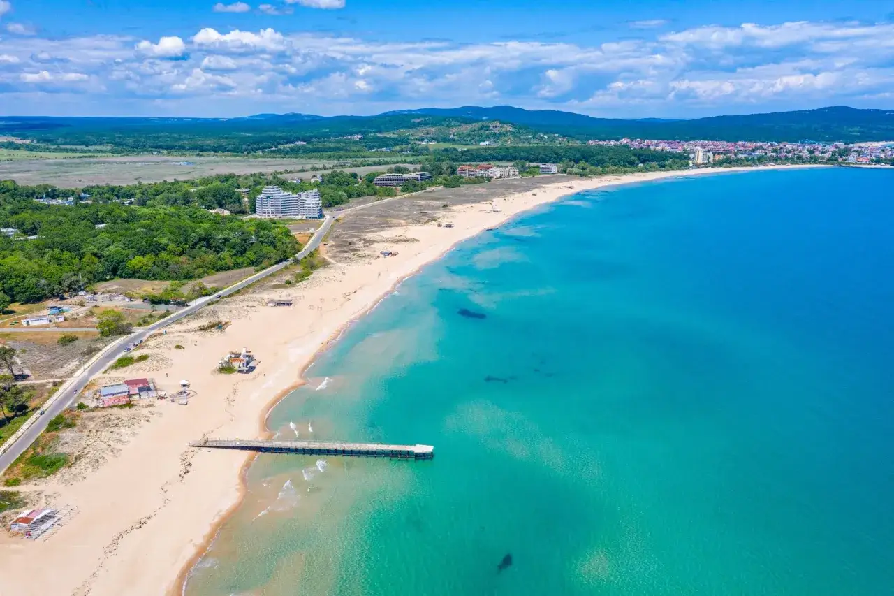 Piękne bułgarskie plaże z turkusową wodą i piaszczystym brzegiem, w tle hotele i zielone wzgórza.