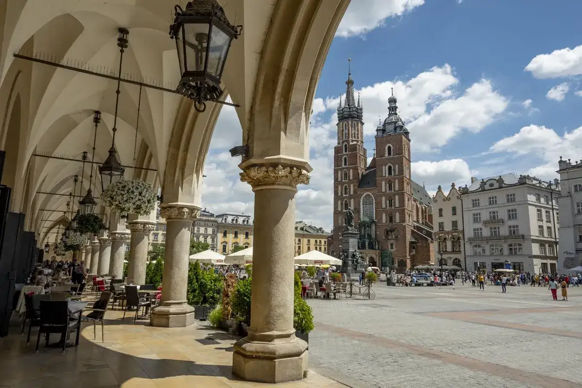 Urokliwe arkady Sukiennic w Krakowie, z widokiem na Kościół Mariacki. Stare miasto w Krakowie tętni życiem.
