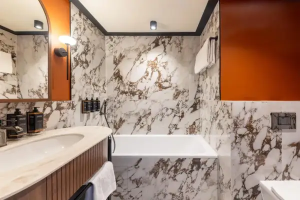 Łazienka w Mercure Gdynia Centrum. Marmurowe ściany, wanna, umywalka i pomarańczowe akcenty. Opinie o hotelu często podkreślają jego nowoczesny design.