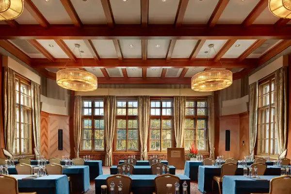 Elegancka sala konferencyjna w Kempinski Hotel, z drewnianymi belkami na suficie, dużymi oknami z widokiem na jesienny krajobraz i dwoma ozdobnymi żyrandolami.