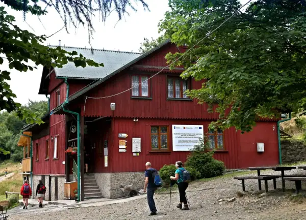 Schronisko PTTK Leskowiec, czerwony budynek w górach, turyści zbliżają się do wejścia.