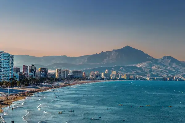 Alicante w grudniu: słoneczna plaża pełna ludzi, turkusowe morze i góry w tle. Idealna pogoda na spacer.