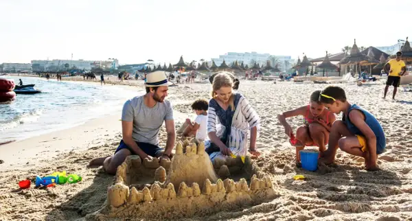 Rodzina buduje zamek z piasku na plaży, idealne miejsce na tunezja wycieczki. Dzieci bawią się z rodzicami, tworząc wspomnienia.
